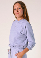 Woman wearing a light gray sweatshirt and pants against a plain background