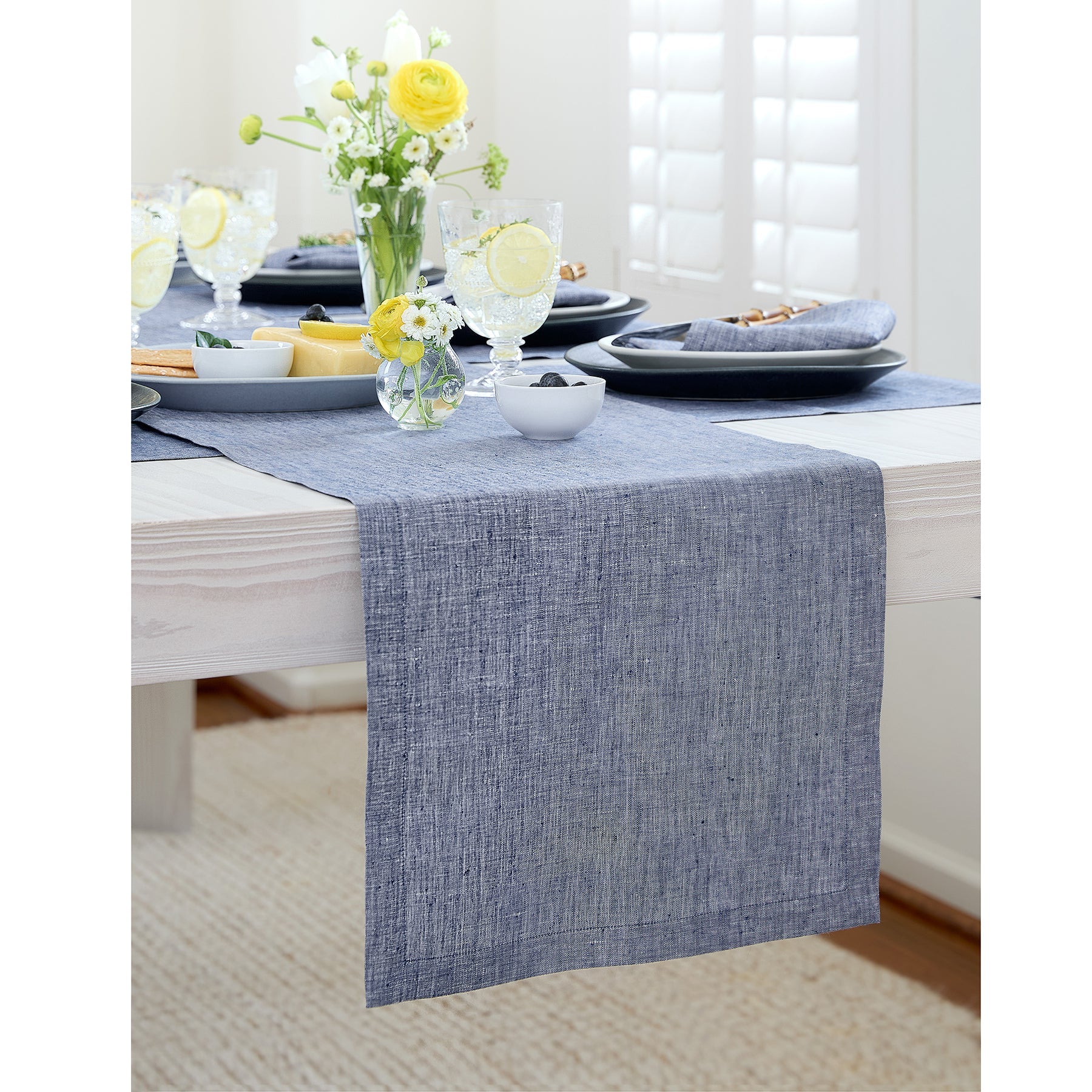 Dining table set with a blue runner, plates, and yellow flowers.