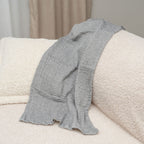 Gray textured blanket draped over a beige sofa with a neutral background