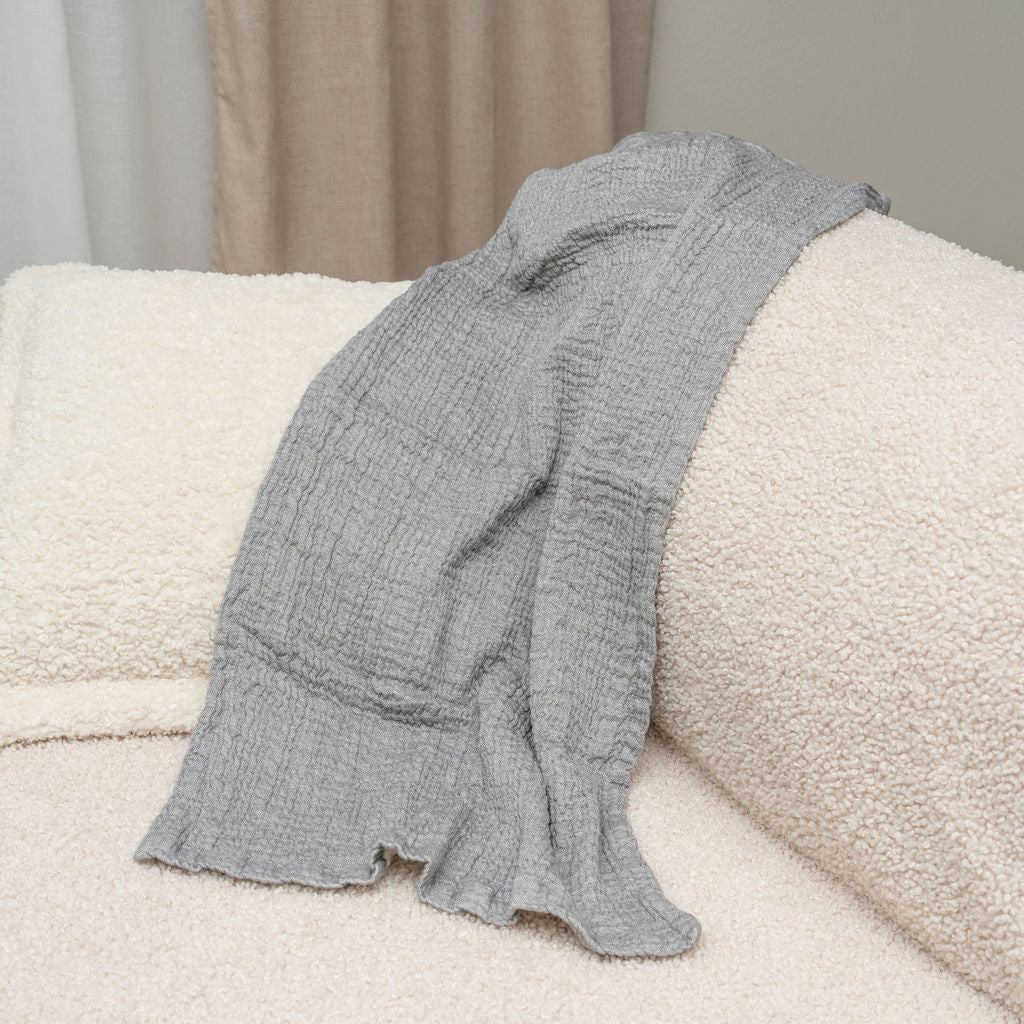 Gray textured blanket draped over a beige sofa with a neutral background